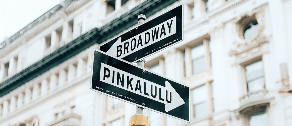 Street sign pointing to 'Broadway' and 'Pinkalulu' with a blurred building background